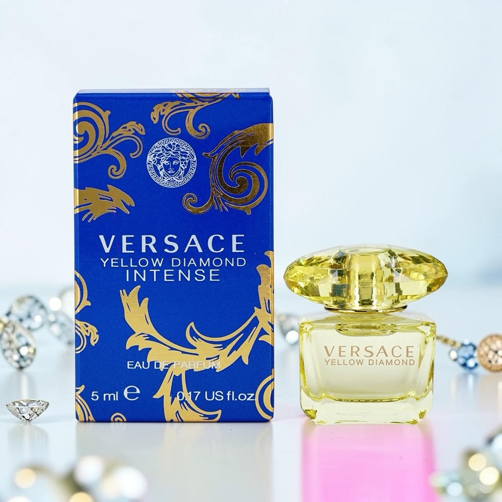 Nevora Versace Yellow Diamond Intense miniature perfume bottle next to its blue and gold box on a reflective surface.